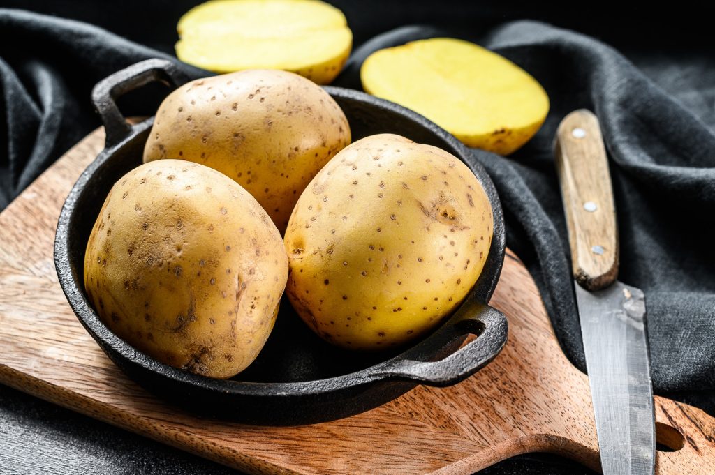 Recipe for fried potatoes, organic yellow potatoes in a pan. Black background. Top view